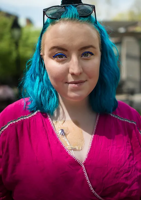 White person with shoulder length blue hair wearing a pink shirt.