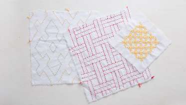 Sashiko stitching example with red and yellow thread on white cloth squares. 