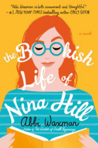 Front cover of The Bookish Life of Nina Hill showing an illustration of a red-haired woman in blue eyeglasses, holding a book and reading it, one eyebrow arched