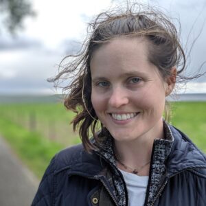 Photo of author Katherine Arden, with a green field behind her and her hair blowing.