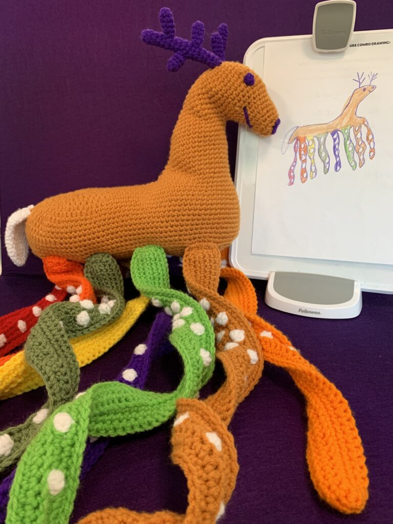 Crochet stuffy based on child's drawing which is also pictured. It's a tan deer with multicolored octopus tentacles.
