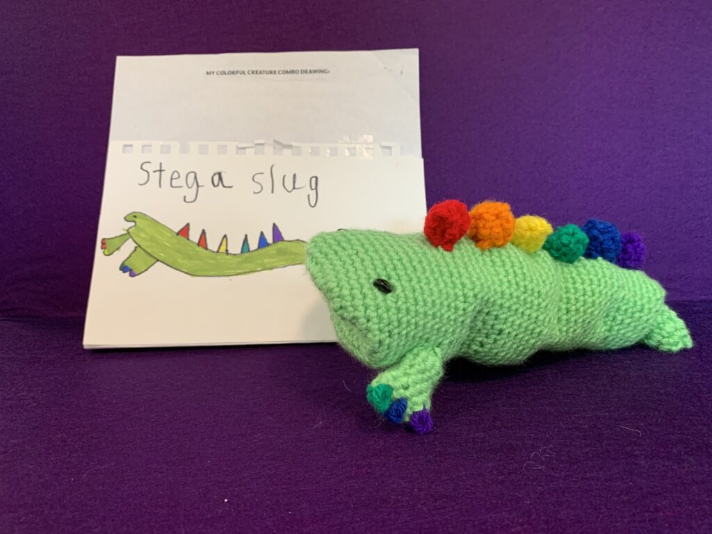 Crochet stuffy based on child's drawing which is also pictured. it's a green slug with rainbow colored spines and toenails.