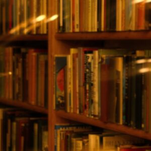 Blurred bookshelves filled with assorted books, illuminated by warm light that creates soft reflections on the surfaces.