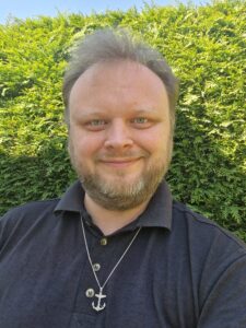 White man with short blond hair and a beard wearing a blue shirt.