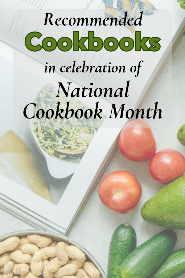 Open cookbook cover displayed on a surface surrounded by fresh tomatoes, cucumbers, an avocado, and a bowl of peanuts.