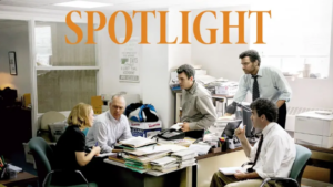 Five people gather around a cluttered office table with scattered papers and folders, as large orange letters above them spell out a word.